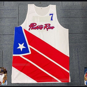 May include: White basketball jersey with red and blue diagonal stripes, a white star, and the text "Puerto Rico" in blue cursive. The number "7" is on the front of the jersey in blue.