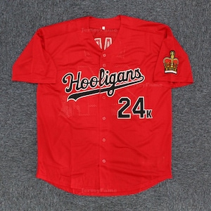 May include: A red baseball jersey featuring the word "Hooligans" in black script and the number "24k". A gold and red crown emblem is on the left sleeve. The jersey has a button-up front. The jersey is red.