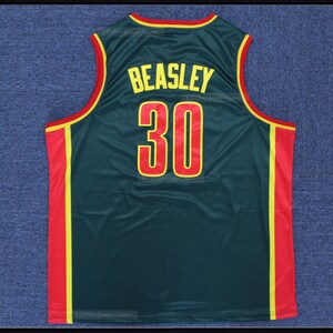 Puede incluir: Una camiseta de baloncesto sin mangas de color verde oscuro con el nombre BEASLEY y el número 30 en amarillo con bordes rojos. La prenda tiene ribetes rojos y amarillos en el cuello y las sisas, con paneles laterales rojos bordeados por rayas amarillas.