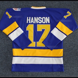 May include: A blue hockey jersey with white and yellow stripes. The number "17" and the name "HANSON" are printed on the back in yellow.
