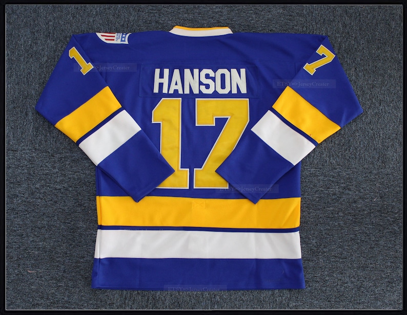 May include: A blue hockey jersey with white and yellow stripes. The number "17" and the name "HANSON" are printed on the back in yellow.