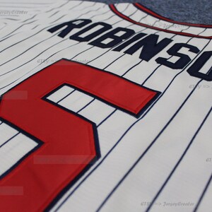 May include: White baseball jersey with blue pinstripes and red number "5" on the front. The name "ROBINSON" is sewn on the back in blue.