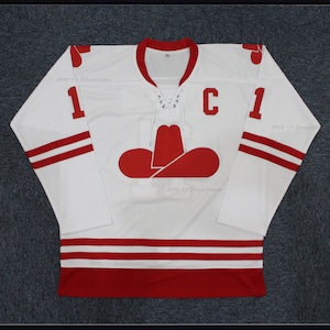 May include: White hockey jersey with red and white stripes. The jersey has a red cowboy hat logo on the front and the number "1" on the sleeves and back. The letter "C" is on the front of the jersey.