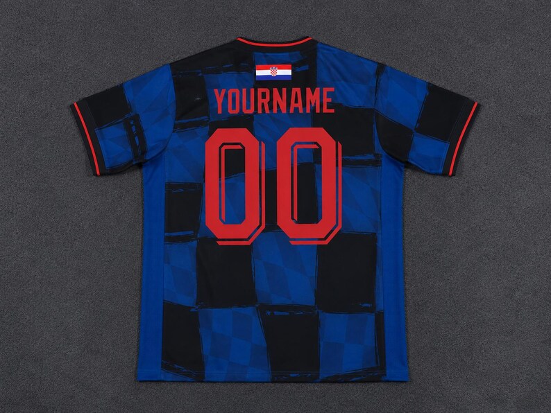 May include: A short-sleeved sports jersey featuring a blue and black checkered pattern. The back displays the red text YOURNAME above the red number 00. A small Croatian flag is positioned at the neckline, and the sleeves have thin red trim.