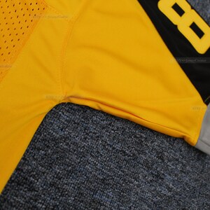 May include: Close-up of a yellow football jersey with black and grey trim. The number 88 is visible on the right shoulder.