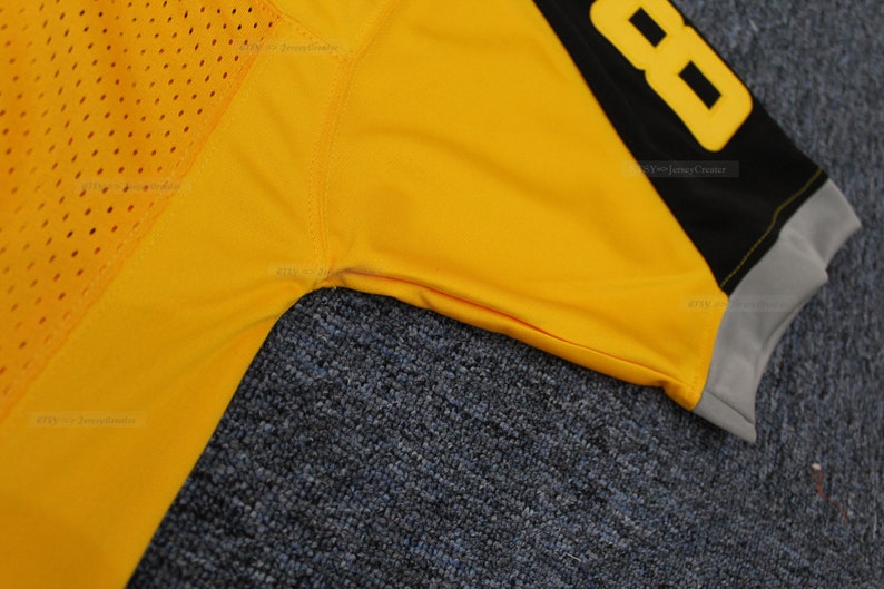 May include: Close-up of a yellow football jersey with black and grey trim. The number 88 is visible on the right shoulder.