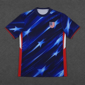 May include: A short-sleeved crew neck t-shirt featuring a dark blue background with a dynamic pattern of light blue diagonal streaks and stars. A small shield-shaped patch with the American flag is on the left chest, with red side panels.