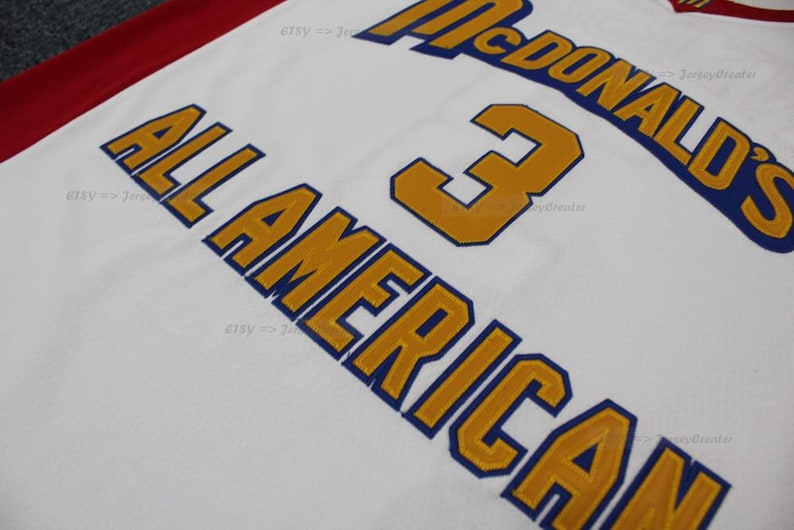 May include: White jersey with gold and blue lettering. The words "McDonald's" and "All American" are visible, along with the number "3". The jersey has a red stripe along the top.