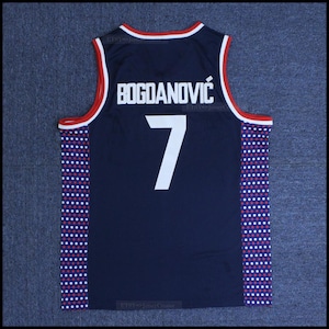 Könnte beinhalten: Ein marineblaues Basketballtrikot mit weißen und roten Tupfen an den Seiten. Auf der Rückseite des Trikots steht der Name "BOGDANOVIC" und die Nummer "7" in Weiß.