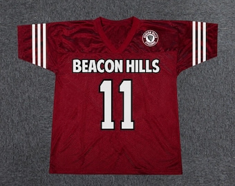 May include: A maroon V-neck jersey with white text reading BEACON HILLS and the number 11 in white. The sleeves feature three white stripes, and a circular logo with the text BEACON HILLS CYCLONES is printed on the upper left chest area.