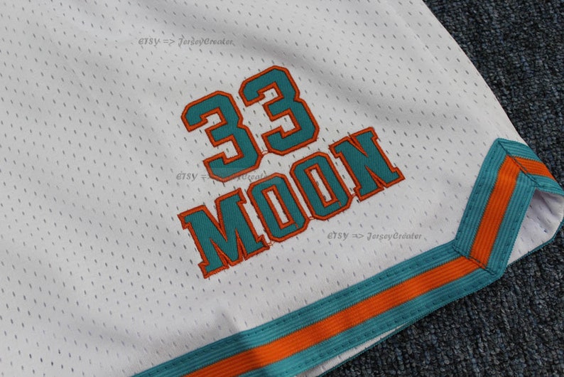 Puede incluir: Pantalones cortos deportivos de malla blanca con detalles en turquesa y naranja. Los pantalones cortos presentan el n&uacute;mero "33" y el nombre "MOON" en turquesa con ribete naranja. El ribete de los pantalones cortos es turquesa y naranja. El nombre de la tienda Etsy "JerseyCreator" es visible.