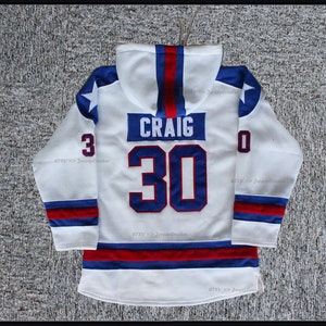 K&ouml;nnte beinhalten: Ein wei&szlig;es Hockeytrikot mit blauen und roten Verzierungen. Das Trikot hat eine Kapuze und die Nummer 30 mit dem Namen "CRAIG" auf der R&uuml;ckseite.