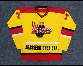 Puede incluir: Jersey de hockey amarillo con detalles rojos y negros. Presenta el texto "Les BOYS" y "BRASSERIE CHEZ STAL" en negro. El número 7 está en cada manga. El jersey tiene cuello en V.