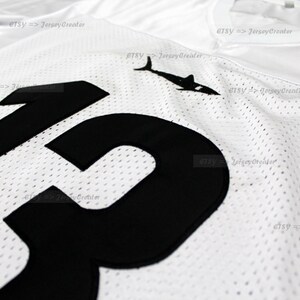 K&ouml;nnte beinhalten: Wei&szlig;es Mesh-Trikot mit einer schwarzen Nummer "13" auf der Vorderseite. Das Trikot hat ein schwarzes Hai-Logo oben links.
