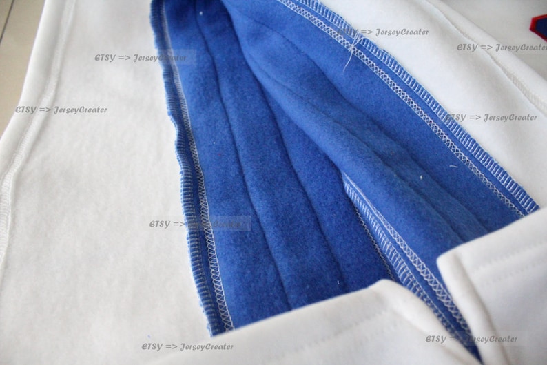 K&ouml;nnte beinhalten: Nahaufnahme des Innenfutters eines wei&szlig;en und blauen Kapuzenpullovers. Das blaue Futter ist sichtbar und zeigt die N&auml;hte und das weiche Fleece-Material.