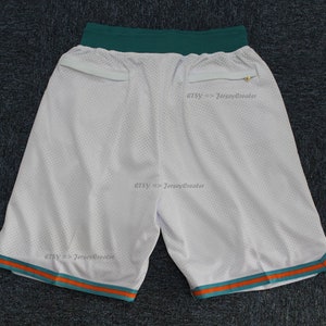 Puede incluir: Pantalones cortos deportivos de malla blanca con ribete turquesa y naranja. Los pantalones cortos tienen una cintura turquesa y dos bolsillos. El texto "Etsy => JerseyCreator" est&aacute; impreso en los pantalones cortos.