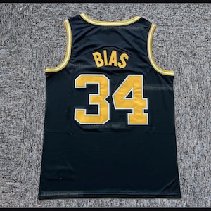 May include: A black sleeveless basketball jersey featuring the name BIAS and the number 34 in yellow with white trim on the back. The neckline and armholes are finished with yellow and white striped ribbed trim, creating a classic athletic look.