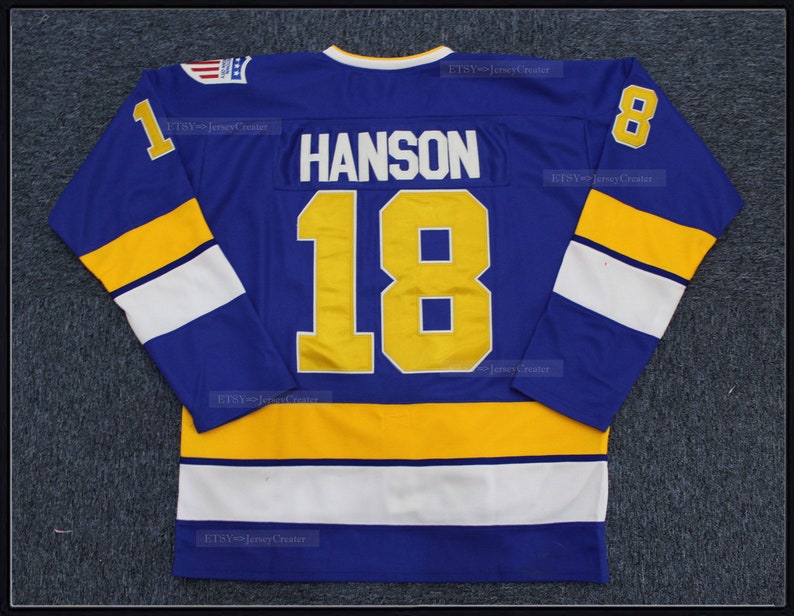 May include: A blue hockey jersey with white and yellow stripes. The number 18 and the name "HANSON" are on the back of the jersey in yellow.