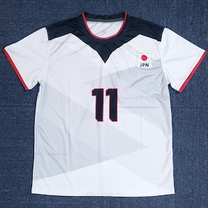 Puede incluir: Camiseta deportiva blanca con detalles en negro y rojo. La camiseta muestra un parche de la bandera japonesa y el número 11 en azul marino. Acentos rojos en las mangas y el cuello. Fabricada con material ligero y transpirable.