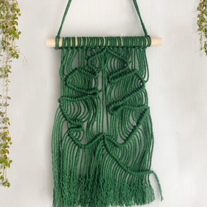 May include: A green macrame wall hanging with a wooden dowel at the top and long fringe at the bottom.