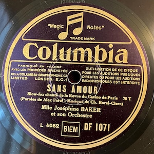 May include: A vintage Columbia record with a dark purple label. The label features gold text and musical notes, with the title "SANS AMOUR" and the artist "Mlle Joséphine BAKER". The record is a 78 RPM, made in France.
