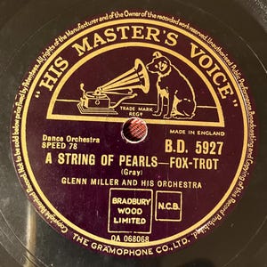 May include: Close-up of a vintage vinyl record with a maroon and gold label. The label features the text "HIS MASTER'S VOICE" and an image of a dog listening to a gramophone. The record is titled "A STRING OF PEARLS - FOX-TROT" by Glenn Miller and His Orchestra.