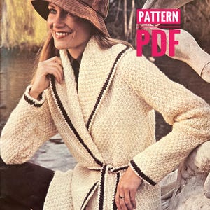May include: Cream-colored knitted coat with dark brown trim and a matching belt. The coat has a shawl collar and is worn with a brown hat. The image also includes the text "PATTERN PDF".