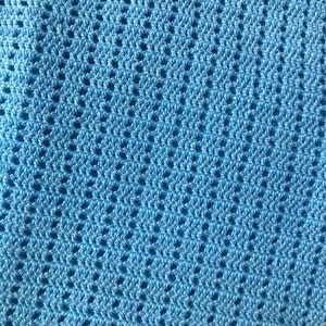 K&ouml;nnte beinhalten: Nahaufnahme einer hellblauen H&auml;keldecke. Die Decke hat ein sich wiederholendes Lochmuster, das eine strukturierte Oberfl&auml;che erzeugt. Die Farbe ist ein weiches, pastellblau, und die Maschen sind gleichm&auml;&szlig;ig verteilt.