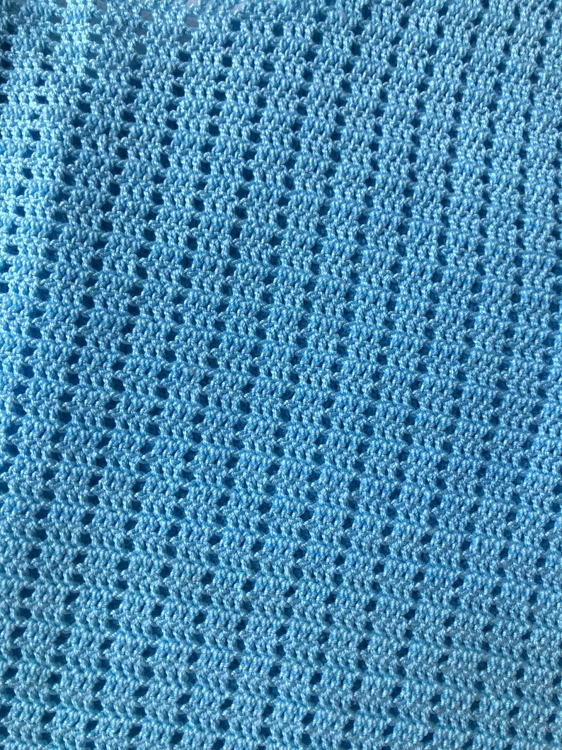 K&ouml;nnte beinhalten: Nahaufnahme einer hellblauen H&auml;keldecke. Die Decke hat ein sich wiederholendes Lochmuster, das eine strukturierte Oberfl&auml;che erzeugt. Die Farbe ist ein weiches, pastellblau, und die Maschen sind gleichm&auml;&szlig;ig verteilt.
