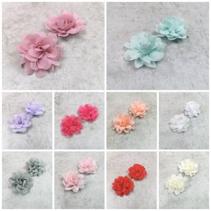 Könnte beinhalten: Set aus zwei kleinen Stoffblumen in verschiedenen Farben, darunter Rosa, Blau, Lavendel, Pfirsich, Rot, Grau und Weiß. Die Blumen bestehen aus weichem, mehrlagigem Stoff und haben ein zartes, gekräuseltes Aussehen.