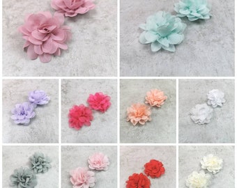 May include: Set of two small fabric flowers in various colors, including pink, blue, lavender, peach, red, gray, and white. The flowers are made of soft, layered fabric and have a delicate, ruffled appearance.