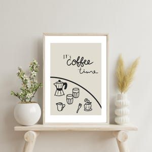 Puede incluir: Una impresión enmarcada con un fondo beige y texto negro que dice "It's coffee time". La impresión presenta una ilustración en blanco y negro de una cafetera, dos tazas, un azucarero y un tenedor.