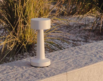 May include: A white, modern table lamp with a round base and a cylindrical shade. The lamp is sitting on a textured, gray surface.