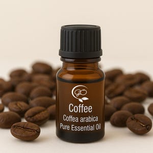以下が含まれることがあります： 黒いキャップが付いた、コーヒーエッセンシャルオイルの小さな茶色のガラス瓶。「Coffee Coffea arabica Pure Essential Oil」と書かれたラベル。コーヒー豆がボトルの周りに散らばっています。