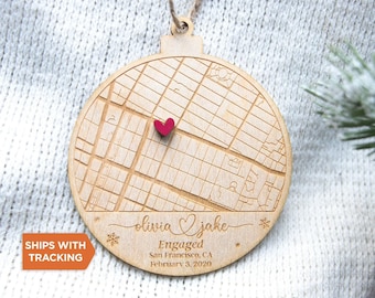 May include: A round wooden ornament featuring an engraved street map of San Francisco, California. A small red heart marks a specific location. The text reads: olivia & jake, Engaged, San Francisco, CA, February 3, 2020, with snowflake icons.