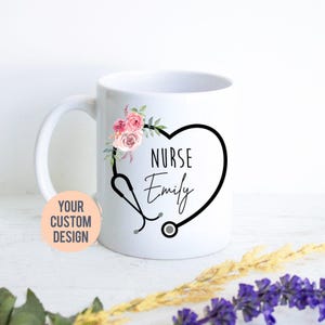 Può includere: Una tazza in ceramica bianca con uno stetoscopio nero a forma di cuore. All'interno del cuore, il testo recita NURSE Emily in carattere nero. Un gruppo di rose acquerellate rosa e pesca con foglie verdi decora il lato superiore sinistro.