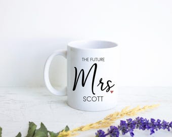 Könnte beinhalten: Ein weißer Keramikbecher mit dem schwarzen Aufdruck "THE FUTURE Mrs. SCOTT" und einem kleinen roten Herzsymbol neben dem Wort "Mrs.". Der Becher verfügt über einen Standardhenkel und eine glatte, glänzende Oberfläche mit klar lesbarer Schrift.