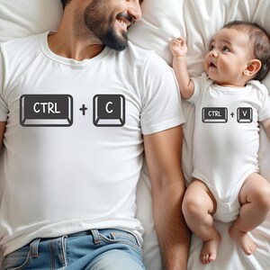 May include: White t-shirts and a onesie with keyboard key graphics. The adult shirt shows "CTRL + C", and the baby's onesie displays "CTRL + V". The matching outfits are designed for a parent and child.