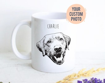 May include: A white ceramic mug featuring a black line art illustration of a dog's face centered on the front. Above the dog illustration, the name CHARLIE is printed in black text. A circular peach-colored badge reads YOUR CUSTOM PHOTO.