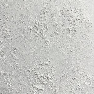 May include: A close-up of a white textured wall with a rough, uneven surface. The wall has a slightly grainy appearance, with small bumps and dips throughout.