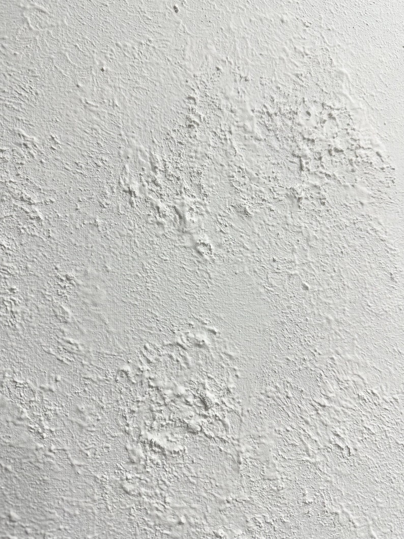 May include: A close-up of a white textured wall with a rough, uneven surface. The wall has a slightly grainy appearance, with small bumps and dips throughout.