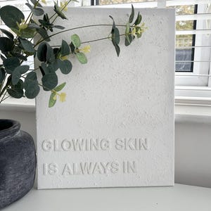 May include: White canvas wall art with the text "Glowing skin is always in" embossed on the surface.