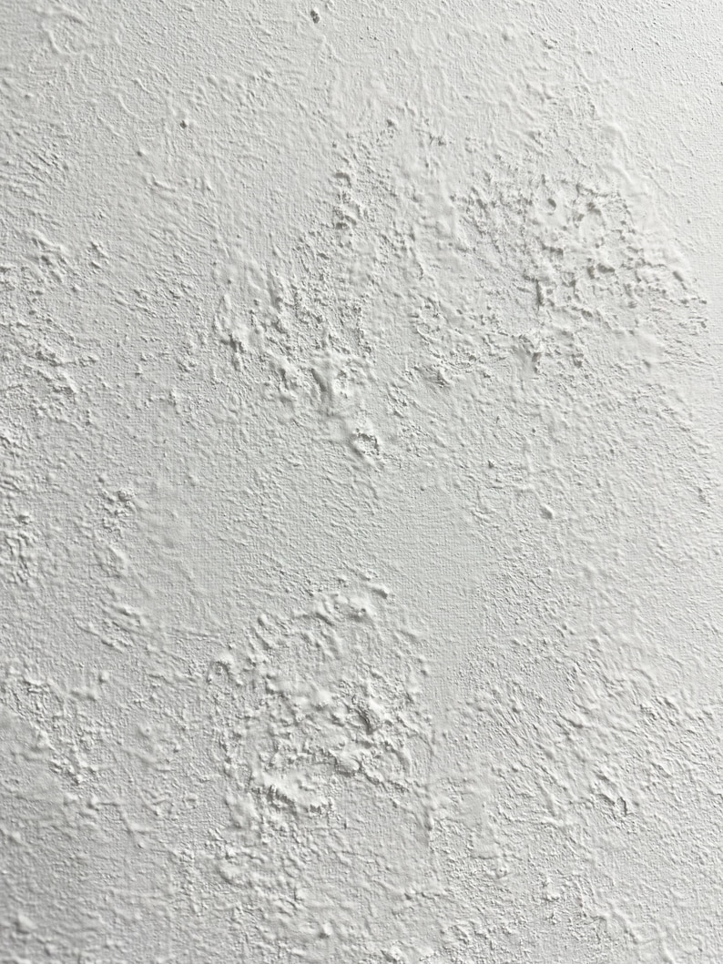 May include: A close-up of a white textured wall with a rough, uneven surface. The wall has a slightly grainy appearance, with small bumps and dips throughout.