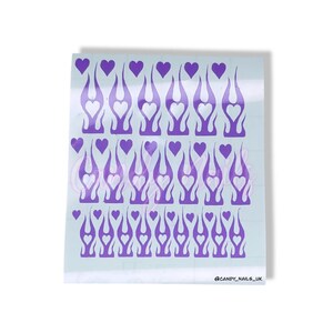 Puede incluir: Una hoja de pegatinas para u&ntilde;as de color morado y blanco con un dise&ntilde;o de llama y un coraz&oacute;n en el centro de cada llama. La hoja tiene 36 pegatinas en total. @CANDY_NAILS_UK