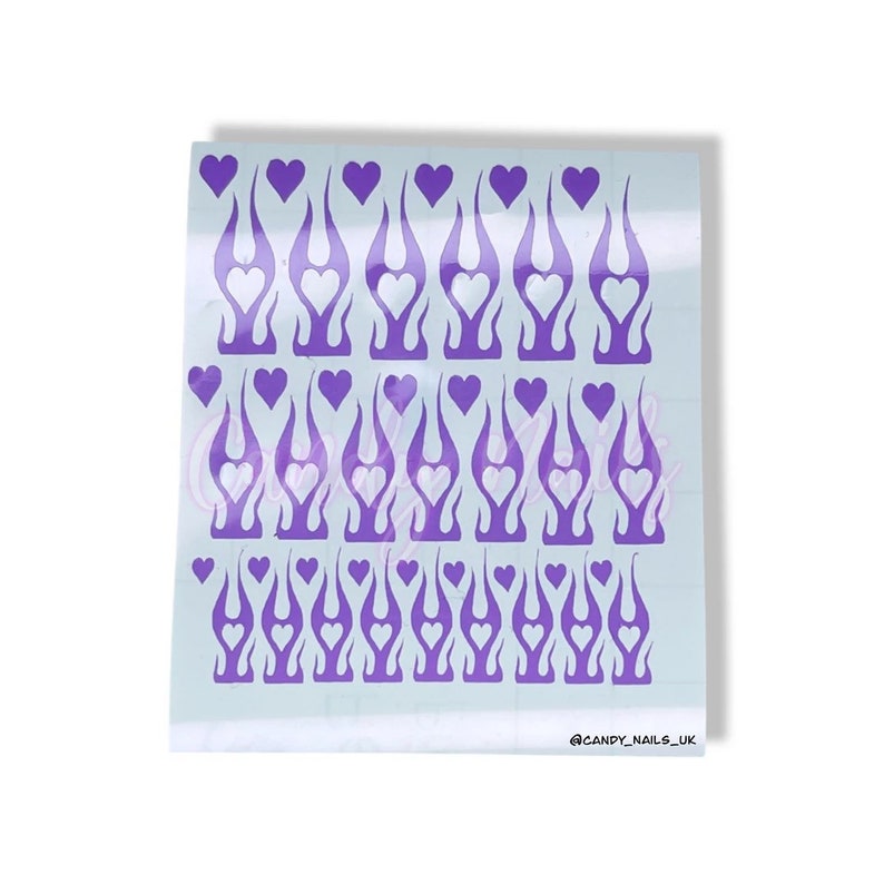 Puede incluir: Una hoja de pegatinas para u&ntilde;as de color morado y blanco con un dise&ntilde;o de llama y un coraz&oacute;n en el centro de cada llama. La hoja tiene 36 pegatinas en total. @CANDY_NAILS_UK
