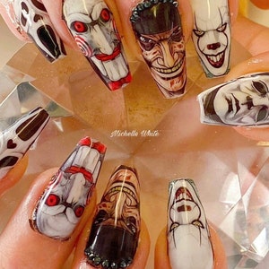 Op de afbeelding: Close-up van lange, amandelvormige nagels met horrorfilm-personage nagelkunst. De nagels zijn beschilderd met afbeeldingen van personages uit horrorfilms, waaronder Pennywise de clown, Freddy Krueger en Michael Myers. De nagelkunst is gedetailleerd en realistisch, met felle kleuren en scherpe details.