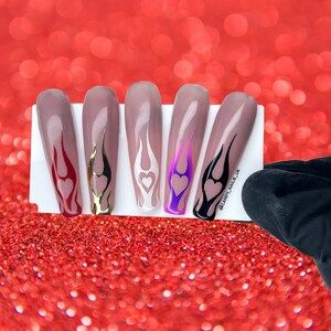 Puede incluir: Cinco u&ntilde;as postizas largas en forma de almendra con dise&ntilde;os de llamas de diferentes colores y un coraz&oacute;n en la punta. Los colores son rojo, dorado, blanco, morado y negro.