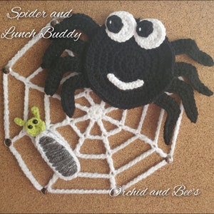 May include: A black crocheted spider with white eyes and a smile sits on a white crocheted spider web. A green and gray crocheted caterpillar is caught in the web. The text "Spider and Lunch Buddy" is above the spider and the text "Orchid and Bee's" is below the web.