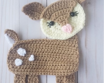 Puede incluir: Un ciervo de crochet marrón con manchas blancas, ojos negros y una nariz rosa. El ciervo está de pie sobre una superficie de madera blanca. El texto "Willow The Baby Deer" está por encima del ciervo. El texto "Orchid and Bee's" está debajo del ciervo.