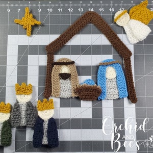 May include: Crocheted nativity scene featuring a brown stable, star, angel, and figures of Mary, Joseph, baby Jesus, and the three wise men. The figures are in shades of brown, blue, white, and gold. The text "Orchid and Bees" is in the bottom right corner.